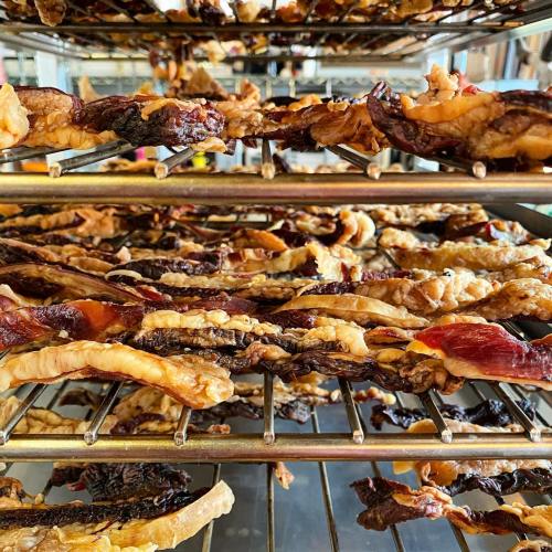 Close-up of drying meat strips on metal racks, showcasing various textures and colors in a food preparation setting.
