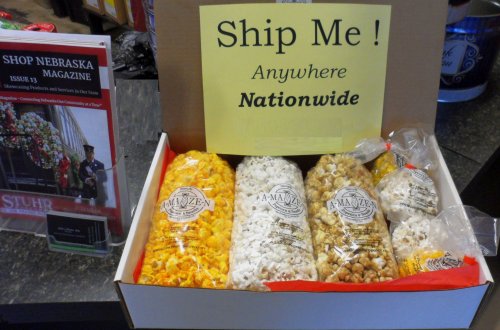A box of popcorn varieties with a sign saying "Ship Me! Anywhere Nationwide" and a magazine on the side.
