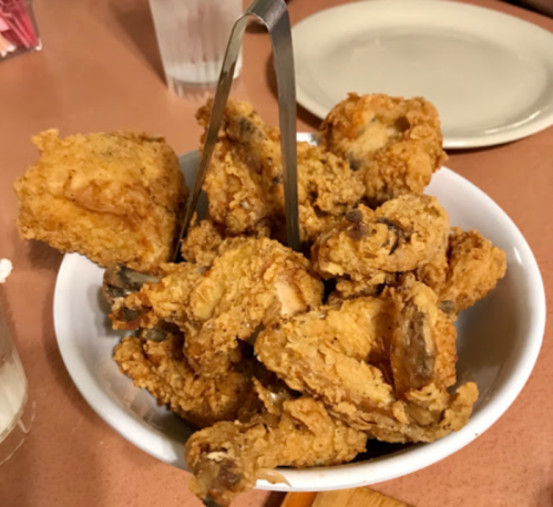 A bowl of crispy fried chicken pieces with a serving tongs resting on top.