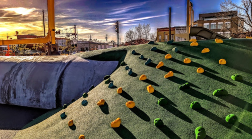Colorful climbing holds on a green hill at a playground, with a sunset sky in the background.