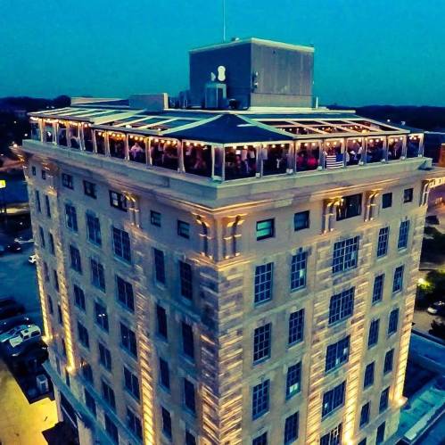 Aerial view of a tall building with a rooftop gathering, illuminated at dusk.