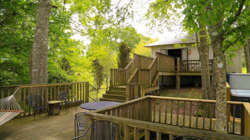 A wooden deck with chairs and a hammock, leading to a house surrounded by lush greenery and trees.