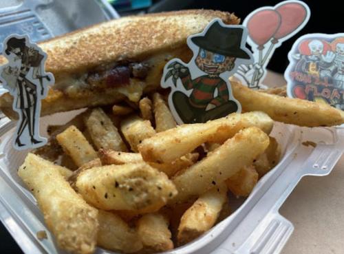 A toasted sandwich with cheese and bacon, served with seasoned fries and cartoon character stickers.
