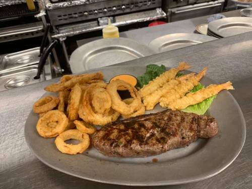 A plate featuring a grilled steak, onion rings, shrimp tempura, and lettuce, set on a kitchen counter.