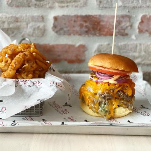 A juicy cheeseburger with melted cheese, onions, and tomato, served with a side of curly fries on a tray.