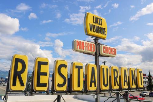 Sign for "Lucky Wishbone" restaurant featuring "Pan-Fried Chicken" against a blue sky with clouds.