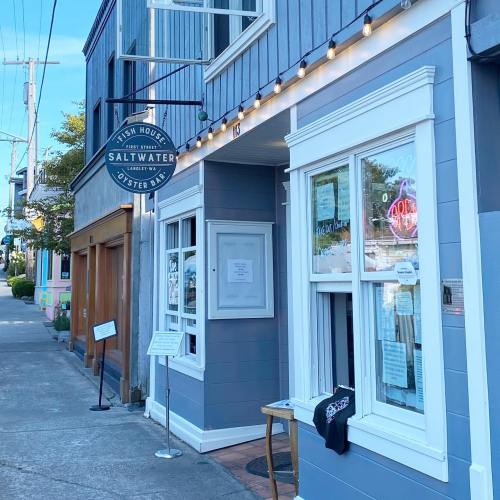 Exterior of Saltwater Fish House, featuring a blue facade, string lights, and a sign, with a sidewalk and nearby buildings.