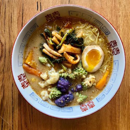 A bowl of ramen with vegetables, an egg, and squid, served in a decorative bowl on a wooden surface.