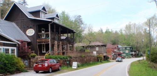 A scenic view of a rural road lined with charming wooden houses and greenery in the background.