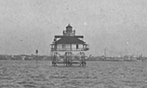 A vintage black-and-white image of a lighthouse on stilts in the water, with a distant shoreline visible.