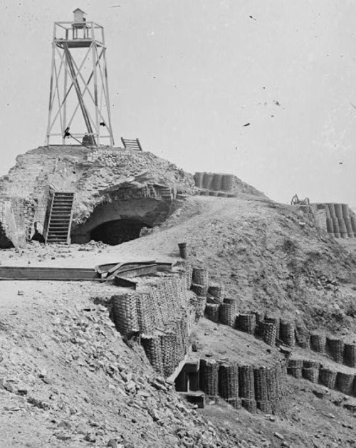 A historical black-and-white photo of a lighthouse on a hill, with steps leading up and baskets stacked along the slope.