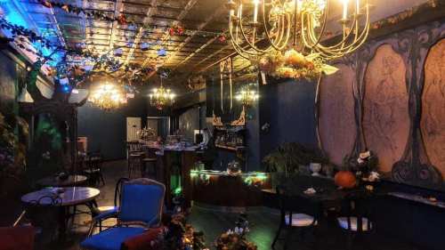 A cozy, elegantly decorated lounge with chandeliers, floral accents, and a bar area, featuring vintage furniture.