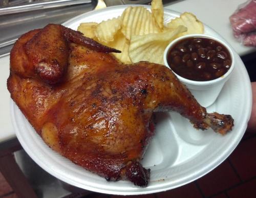 A plate with a smoked chicken, crinkle-cut fries, and a small cup of baked beans.