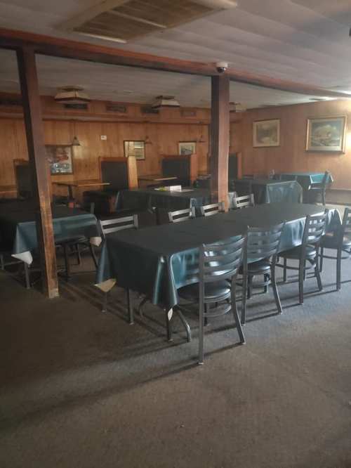 Empty restaurant interior with wooden paneling, tables covered in dark green cloths, and a few paintings on the walls.