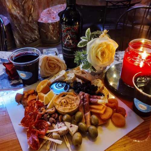 A beautifully arranged charcuterie board with meats, cheeses, fruits, and a bottle of wine, surrounded by candles and flowers.