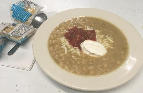 A bowl of white bean soup topped with salsa and sour cream, served with crackers on the side.