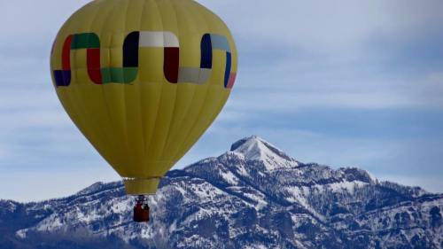 A colorful hot air balloon floats above snow-capped mountains under a clear sky.