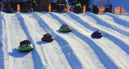 A snowy hill with people tubing down in colorful inflatable tubes, surrounded by festive decorations.