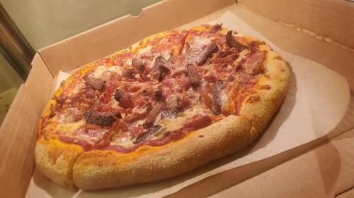 A freshly baked pizza with toppings of meat and cheese, placed in a pizza box.