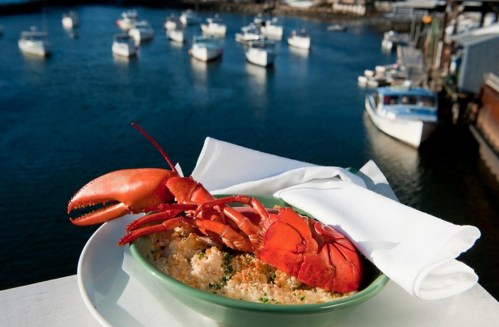 A plate of lobster on a green dish, with boats in the water and a harbor in the background.