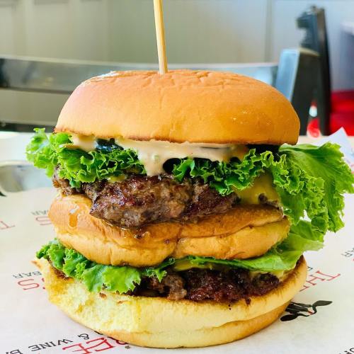 A towering burger with two beef patties, lettuce, cheese, and sauce, served on a soft bun.
