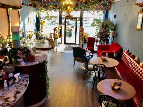 A cozy café interior with floral decor, wooden tables, and a mix of vintage chairs, bathed in natural light.