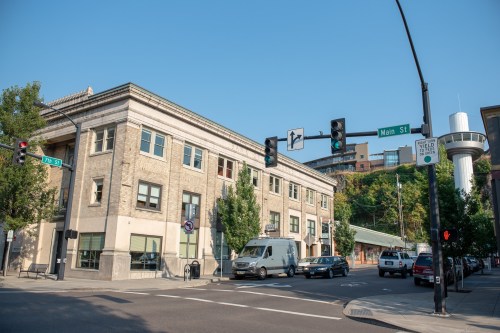 A street view of a historic building at the corner of Main St and another street, with traffic lights and greenery.