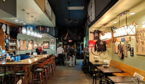 A cozy bar interior with wooden stools, hanging lights, and walls decorated with bicycles and vintage photos.