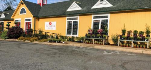 A bright yellow building with a green roof, featuring flower beds and a sign, surrounded by a parking area.