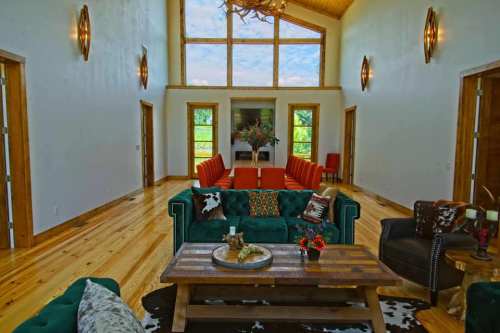 Spacious living room with wooden floors, green sofa, wooden coffee table, and large windows letting in natural light.