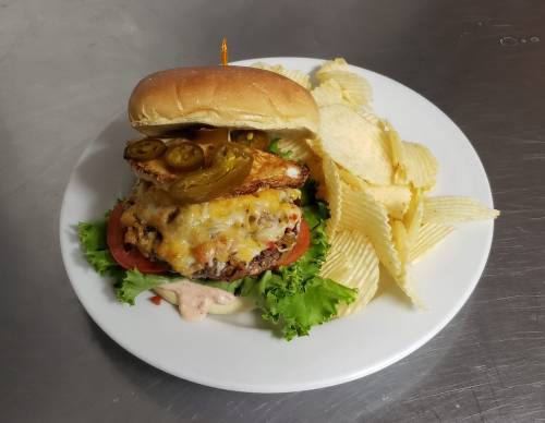A juicy burger topped with cheese, jalapeños, and lettuce, served with potato chips on a white plate.