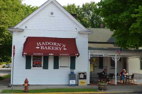 A quaint bakery with a red awning reading "Hadorn's Bakery," featuring outdoor seating and a fire hydrant nearby.