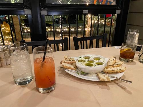 A table setting with a plate of bread and dipping oil, a cocktail, and a glass of water in a cozy restaurant.
