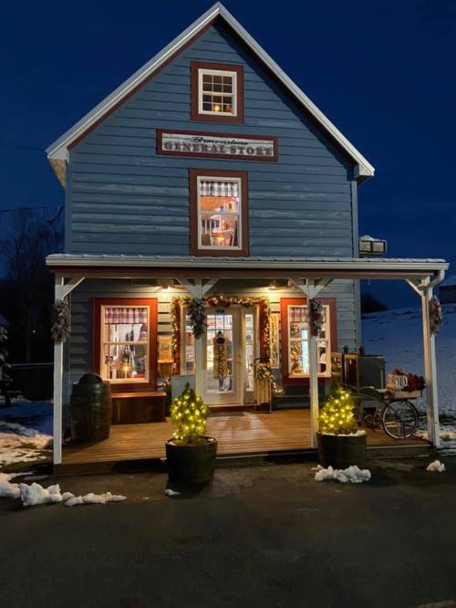 A charming blue house with festive decorations and glowing lights, set against a twilight sky. Snow is on the ground.