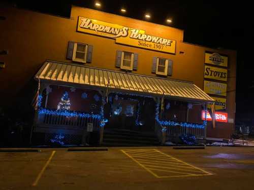 A hardware store at night, decorated with holiday lights and a small Christmas tree outside.