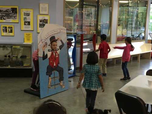 Children playing in a museum, interacting with a colorful display featuring a seated character.