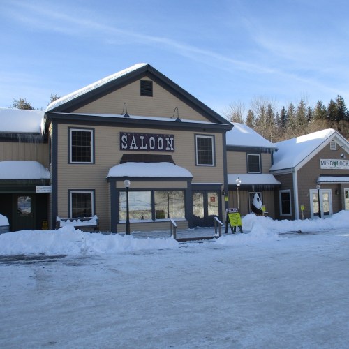 A snow-covered building with a large "SALOON" sign, surrounded by a winter landscape.