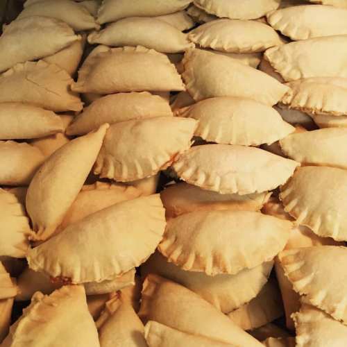 A close-up of numerous golden-brown, crescent-shaped pastries stacked closely together.