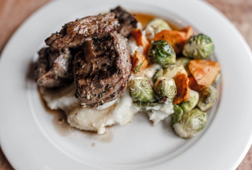 A plate of grilled steak served with mashed potatoes and a medley of roasted Brussels sprouts and vegetables.