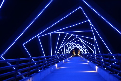 A futuristic bridge illuminated with blue lights, creating a spiral effect against a dark background.