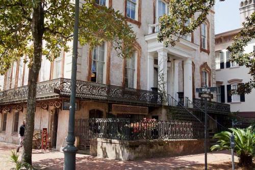 Historic building with ornate ironwork, surrounded by greenery and street signs, showcasing classic architecture.