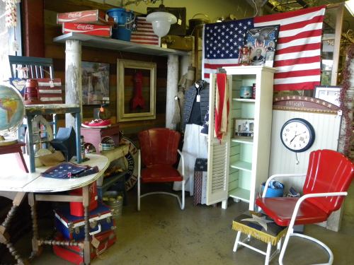 A vintage shop corner featuring red chairs, an American flag, and various eclectic decor items.