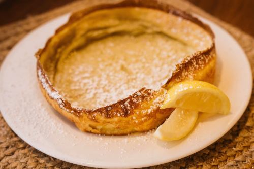 A fluffy Dutch baby pancake dusted with powdered sugar, served with a lemon wedge on a white plate.