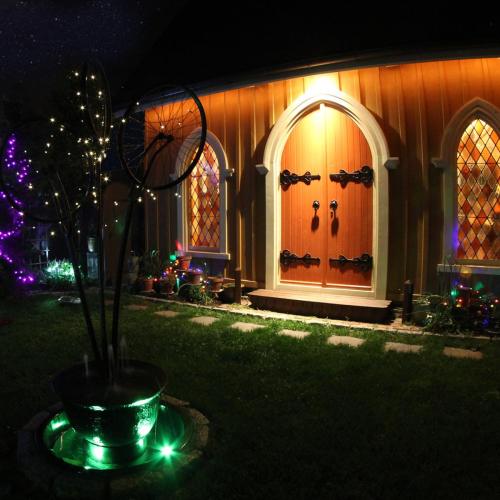 A cozy, warmly lit house with decorative windows and a vibrant garden, adorned with colorful lights.