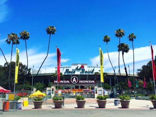 The Rose Bowl stadium entrance with palm trees and colorful flags under a clear blue sky.