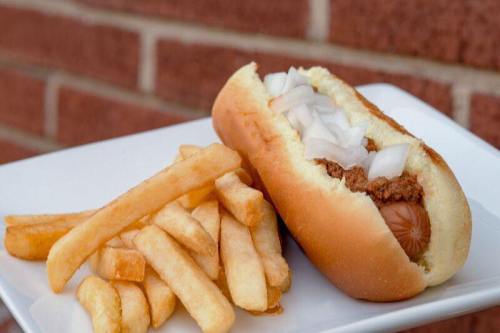 A hot dog topped with chopped onions, served on a plate with a side of golden French fries.