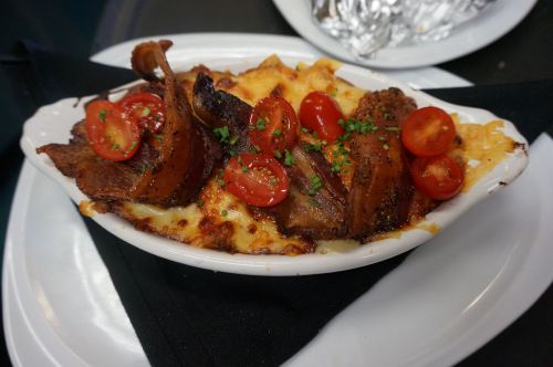 A baked dish with creamy cheese, topped with crispy bacon and cherry tomatoes, served on a black napkin.