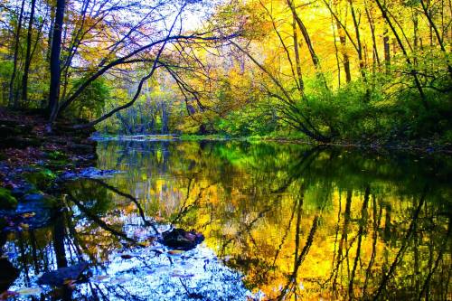 A serene river scene surrounded by vibrant autumn foliage, with colorful reflections on the water's surface.