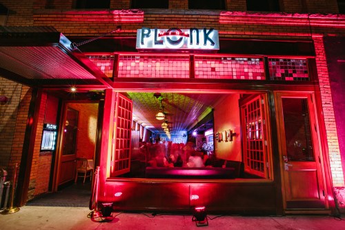 Exterior of Plonk restaurant, featuring vibrant pink lighting and a lively atmosphere visible through large windows.