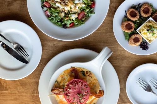 A table set with a salad, a dish of baked eggs topped with bacon and tomato, and small servings of appetizers.